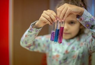 Dziecko trzymające trzy fiolki z różnymi kolorami płynów.