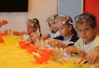 Czworo dzieci siedzących przy stole z przedmiotami potrzebnymi do eksperymentów. Na głowie mają założone gogle.
