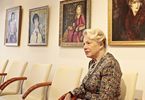 Kobieta siedzi na krześle i pozuje na tle wystawy portretów