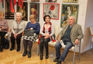 Seniorki i senior siedzący na krzesłach w pomieszczeniu z kolorowymi obrazami
