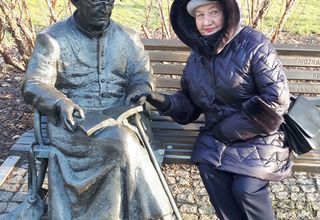 Kobieta siedzi przy pomniku ks. Jana Twardowskiego