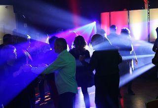 Grupa ludzi tańczy na sali. Tłum oświtlony kolorowymi światłami.