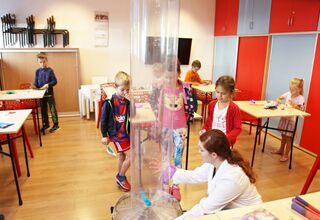 Kobieta pokazuje dzieciom eksperyment z wiatrakiem oraz wysoką plastykową tubą