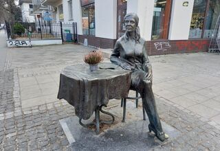 Pomnik: kobieta w średnim wieku siedzi przy okrągłym stole.