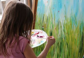 Dziewczynka maluje akwarelami obraz przedstawiający łąkę