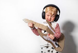 Dziecko ze słuchawkami na uszach grające na gitarze wyciętej z tektury