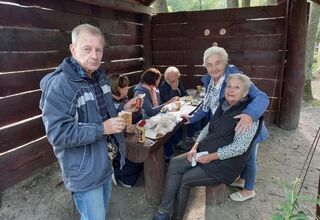 Seniorzy jedzą przez siebie upieczone na ognisku kiełbaski