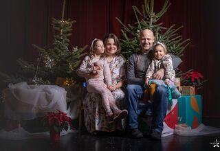 Rodzina pozująca do zdjęcia na świątecznym tle w formie choinek z lampkami, prezentów, siedzący na świątecznym fotelu i pufach DK Zacisze
