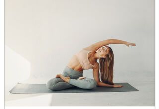 Kobieta podczas rozciągania, trzymająca dłoń e górze, siedząca po turecku na macie do yogi