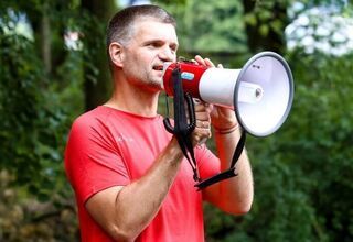 Mężczyzna w czerwonej koszulce przemawiający przez megafon