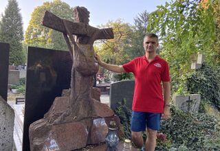 Zdjęcie: Mężczyzna w czerwonej koszulce przy nagrobku w kształcie plecaka, w tle drzewa