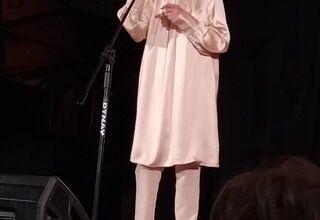 Kobieta ubrana w beżowe spodnie i tunikę na scenie