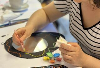 Zdjęcie: kobieta malująca czarną ramkę lusterka żółtymi kropkami farby, obok leżące ozdobione lusterko w technice dots