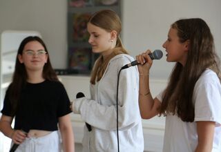 Zdjęcie: trzy dziewczyny z mikrofonami w ręce, jedna śpiewająca