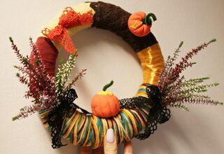 Zdjęcie: wielokolorowy wianek z bukietami wrzosów przewiązany kokardką z miniaturowymi dyniami trzymany w kobiecej dłoni