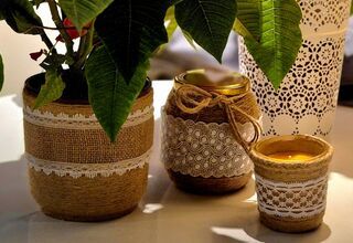 Zdjęcie: świecznik ozdobiony jutą i koronką na tle doniczki i słoika udekorowanych jutą