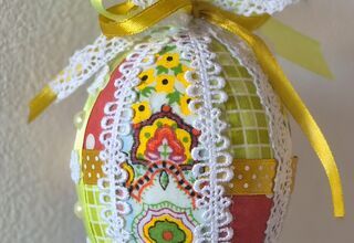 Zdjęcie: Pisanka w żółto-białej kolorystyce z czerwonymi akcentami ozdobiona kolorowymi skrawkami tkanin, koronką, wstążkami oraz koralikami