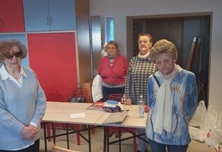 Zdjęcie czterech osób starszych i jednej młodszej stojących przed stołami