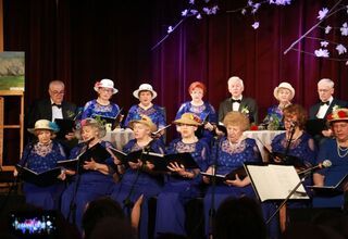 Zdjęcie kobiet na scenie w niebieskich sukienkach w kapeluszach, mężczyzn w garniturach