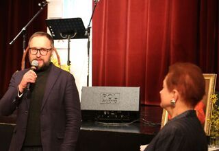 Zdjęcie mężczyzny trzymającego mikrofon, obok siedząca kobieta