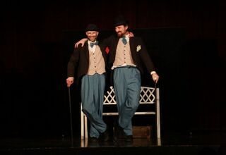 Zdjęcie: dwóch uśmiechniętych mężczyzn na scenie trzymających się za ramię, z tyłu biała ławeczka