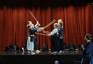 Zdjęcie: Sześcioro dzieci z mieczami drewnianymi na scenie, podczas pokazu kendo