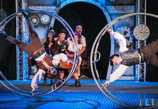 Zdjęcie: grupa osób wykonujących pokaz akrobatyczny na wielkich kołach w steampunkowej scenografii
