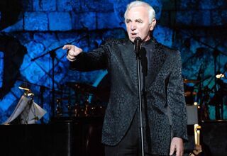 Zdjęcie starszego człowieka z podniesioną ręką, foto: https://jazzforum.com.pl/main/news/charles-aznavour-po-blisko-30-latach-znowu-w-polsce