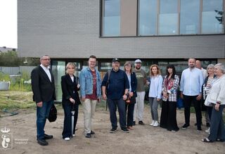 Zdjęcie: dwanaście osób, kobiety i mężczyźni przed budynkiem obłożonym szarym klinkierem, z dużymi oknami, źródło: Urząd Dzielnicy Targówek