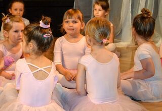 Zdjęcie: grupa dziewczynek w strojach baletowych siedzących po turecku na podłodze