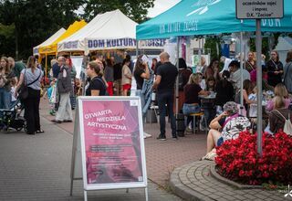 Zdjęcie: wydarzenie plenerowe, 4 namioty, osoby przy stoiskach warsztatowych, na środku na kostce potykacz z nazwą Otwarta Niedziela Artystyczna