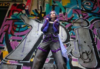 Zdjęcie: nastolatka w stroju hip hopowym, trzymająca bezrękawnik, w tle ściana z graffiti