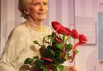 Kobieta stoi na scenie i trzyma róże