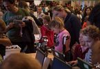 Grupa dzieci i forosłych ogląda sprzęt elektroniczny