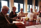 Grupa starszych ludzi siedzi przy stole i śpiewa piosenki