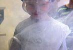 Chłopczyk ubrany w ochronną folię i gogle ochronne schowany za chmurą dymu
