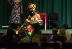 Kobieta w kolorowej sukni i turbanie ozdobionym owocami tańczy przed sceną