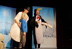 Kobieta przebrana za bałwanka i kobieta w stroju pingwina występują na scenie. Obok stoi dziewczynka.