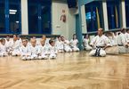 Dzieci i mężczyzna w strojach do karate siedzą na podłodze