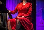Kobieta w czerwonej sukience siedzi przed mikrofonem i śpiewa