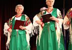 Dwie kobiety w długich spódnicach i ludowych chustach występują na scenie