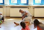 Kobieta pokazuje dzieciom ćwiczenie na podłodze
