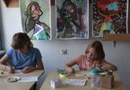 Dwie dziewczynki malują obrazki. Za nimi wiszą trzy obrazy.