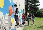 Grupa dzieci tworzy graffiti. Mężczyzna stoi i obserwuje ich pracę.