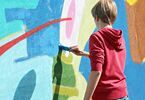 Chłopiec w bluzie maluje mural