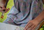 Dziewczynka przykleja naklejkę na drewnianą tabliczkę z motylkiem