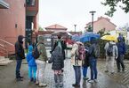 Grupa ludzi stoi przed budynkiem w deszczu