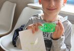 Chłopiec trzyma kartkę, pojemnik z zieloną substancją oraz mały papierek