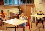 Czworo dzieci siedzi przy stolikach. Chłopiec trzyma fiolki i pozuje do zdjęcia.