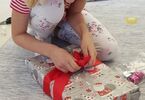 Dziewczynka wiążąca kokardkę na prezencie świątecznym